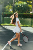 stylish woman with long brunette hair walking in sporty white outfit and holding racket with ball on tennis court in Miami, Florida, Sunny day, blurred palm trees on background, iconic city  mug #658652618