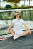 training on tennis court in Miami, beautiful young woman with brunette long hair sitting in sporty white outfit and sunglasses near racket, tennis net, blurred background, iconic city  hoodie #658652974