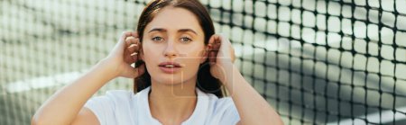 joueuse assise sur un court de tennis, jeune femme sportive aux cheveux longs brune assise en tenue blanche près d'un filet de tennis, fond flou, Miami, regardant caméra, bannière 