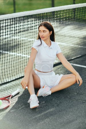 kobieta tenisistka odpoczywająca po grze, młoda kobieta z brunetką długie włosy siedzi w białym stroju i buty w pobliżu rakiety, piłka i siatkę tenisową, niewyraźne tło, Miami, kultowe miasto, kort tenisowy 
