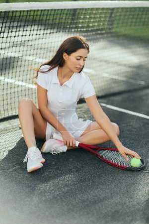 jugadora de tenis que descansa después del partido, mujer joven con el pelo largo sentado en traje blanco y la celebración de raqueta con pelota cerca de la red de tenis, fondo borroso, Miami, ciudad icónica, pista de tenis 