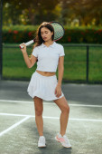 vacation concept, athletic young woman with brunette long hair standing in white outfit, skirt and polo shirt while holding racket in tennis court in Miami, Florida, female player, travel magic mug #658653810