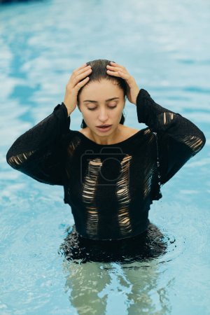 sans maquillage, belle et sexy femme en tricot noir posant à l'intérieur de la piscine extérieure pendant les vacances à Miami, séduisante, station de luxe, beauté naturelle 
