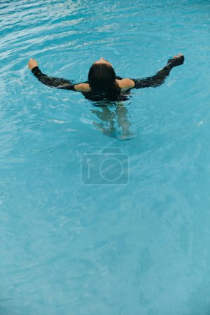 escapada de verano, mujer morena despreocupada nadando en el agua azul de la piscina pública en el complejo de lujo en Miami, agua brillante, libertad, relajación, resort en Miami 