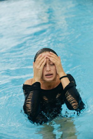 resort de lujo en Miami, hermosa mujer con piel bronceada tocando su cara mojada después de nadar en la piscina pública, posando y disfrutando de sus vacaciones de verano, sin maquillaje 