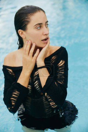 Luxus-Resort in Miami, sonnengebräunte Frau mit gebräunter Haut, die ihr nasses Gesicht berührt, nachdem sie im öffentlichen Schwimmbad geschwommen ist, posiert und ihren Sommerurlaub genießt, ohne Make-up-Look 