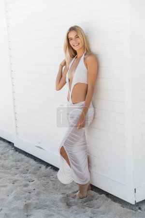 Foto de A young blonde woman standing gracefully next to a clean white wall in Miami Beach. - Imagen libre de derechos