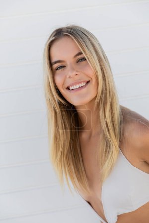 Eine junge blonde Frau in weißem Top lächelt strahlend vor der Kulisse von Miami Beach.