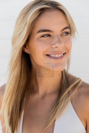 A young blonde woman with long hair smiles warmly at the camera on a sunny day at Miami Beach.