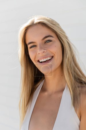 Téléchargez les photos : Une jeune et belle blonde à Miami Beach, vêtue d'un haut blanc, sourit chaudement à la caméra. - en image libre de droit