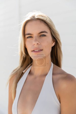 Une belle jeune femme aux cheveux blonds pose avec confiance dans un haut blanc à Miami Beach, exsudant grâce et charme.
