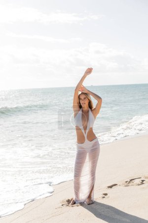 Une jeune femme blonde se tient gracieusement sur le rivage sablonneux de Miami Beachs, embrassant la solitude paisible autour d'elle.