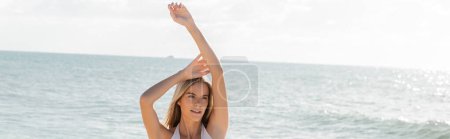 A young blonde woman stands gracefully on Miami beach sandy shore, embracing the peaceful solitude, banner