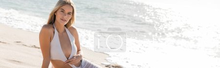 Une jeune femme blonde respire la sérénité dans un bikini blanc sur la plage ensoleillée de Miami, incarnant détente et beauté naturelle.