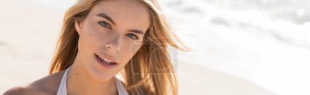 Une jeune, belle femme blonde posant dans un haut de bikini sur une plage de sable fin de Miami sous le soleil éclatant, respirant la confiance.