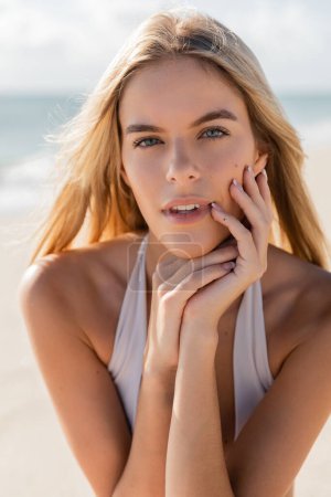 Eine junge blonde Frau posiert am Miami Beach, die Hände vor dem Gesicht, tief in Gedanken und Kontemplation.