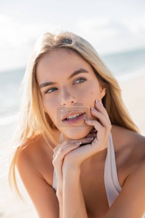 Eine bezaubernde blonde Frau posiert anmutig am sonnenverwöhnten Strand von Miami und strahlt Gelassenheit und Eleganz aus.