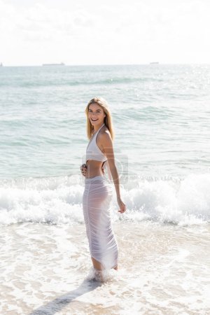 Una joven y hermosa mujer rubia de pie en el agua en Miami Beach en un día soleado.