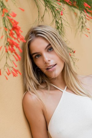 A young, blonde woman in a white top leans gracefully against a wall in a Miami setting.