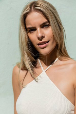 Eine atemberaubende blonde Frau posiert anmutig in einem weißen Top und strahlt vor Miami-Kulisse Eleganz und Stil aus.