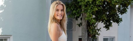Téléchargez les photos : A young, beautiful blonde woman standing confidently in front of a vibrant blue building in Miami. - en image libre de droit