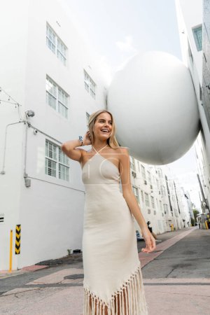 Foto de Una joven rubia en un vestido blanco que fluye cerca de una gran bola blanca, exudando belleza y gracia. - Imagen libre de derechos