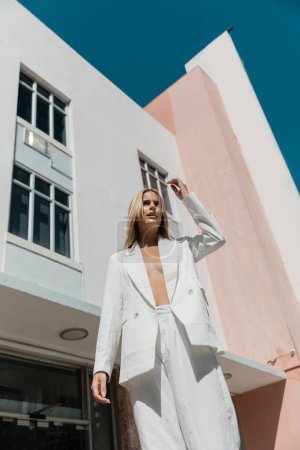 Téléchargez les photos : Une jeune, belle femme blonde debout gracieusement devant un bâtiment rose et blanc vibrant à Miami. - en image libre de droit