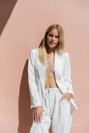 Téléchargez les photos : A young blonde woman in a white suit stands gracefully next to a vibrant pink wall in Miami. - en image libre de droit