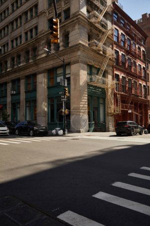 Foto de Edificio de esquina con escaleras de escape de incendios y coches en cruce en la calle del centro de la ciudad de Nueva York - Imagen libre de derechos