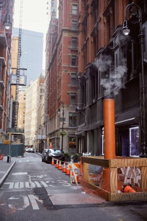 Lüftungsrohre dampfen neben Autos auf schmaler Fahrbahn in New York City, Großstadtatmosphäre