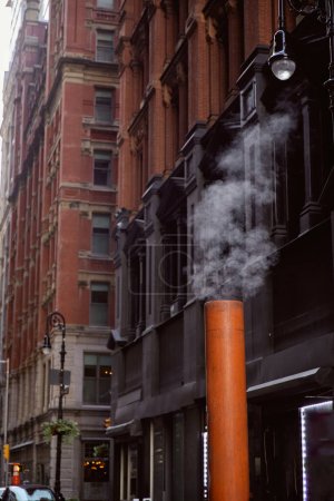 dampfende Lüftungsrohre in der Nähe von Steingebäuden in der Innenstadt von New York City, Straßenszene