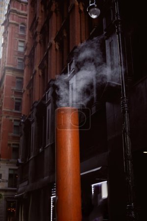 steaming ventilation pipe on street near stone buildings on blurred background in new york city
