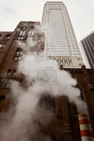 low angle view of red brick catholic church and skyscraper near steam on street in new york city