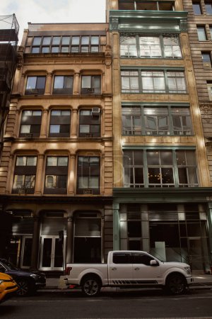 calle de Nueva York con coches modernos que se mueven en la carretera a lo largo de edificios de piedra con grandes ventanales