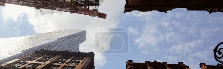 vista inferior de edificios modernos y antiguos contra el cielo azul nublado en la ciudad de Nueva York, bandera
