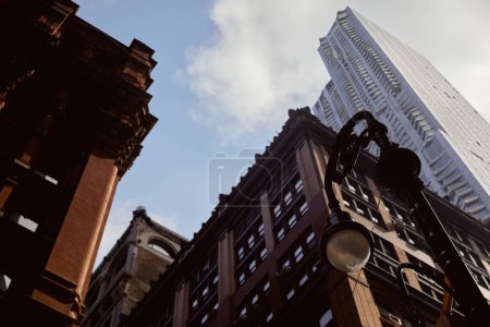 Niedrigwinkel-Ansicht der Laterne in der Nähe moderner und historischer Gebäude gegen blauen bewölkten Himmel in New York City