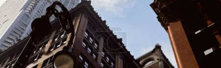sztandar, niski kąt widzenia latarni w pobliżu nowoczesnych i zabytkowych budynków przed niebem w Nowym Jorku
