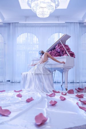 Foto de Hermosa mujer con piano blanco y flores de peonías en estudio blanco - Imagen libre de derechos