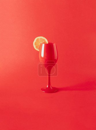Red wine glass with slice lemon on red background. Minimal party concept. Monochromatic invitation background.