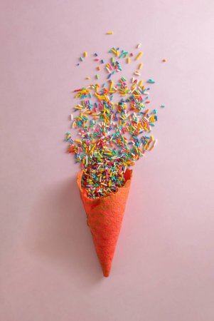 Téléchargez les photos : Cône de crème glacée rouge avec des miettes olores sucrées sur fond violet pastel. Composition minimale de la couche plate d'été. - en image libre de droit