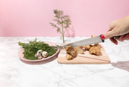 Hand halten Messer, Wachteleier, Dill und Artischocke auf der Küchenoberfläche. Konzept für gesunde Rohkost