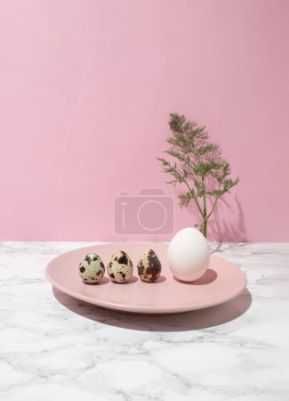 Chicken egg and quail eggs on pink plate on kitchen marble background. Healthy raw food concept