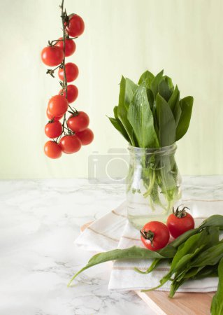 Ramson y los tomates cherry sobre la superficie de trabajo de mármol en la cocina. Concepto de comida saludable
