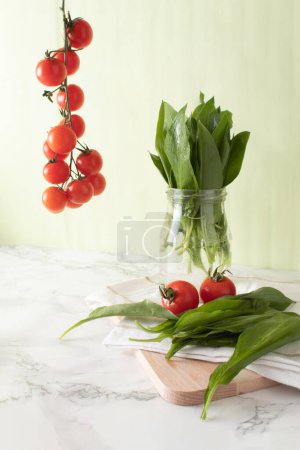 Photo for Ramsons and cherry tomatoes on marble work surface in a kitchen. Healthy food concept - Royalty Free Image