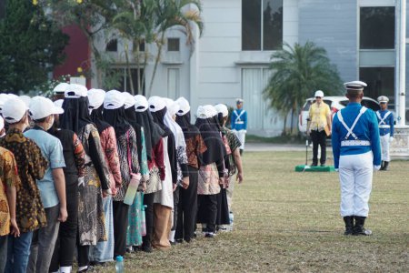 Foto de Estudiantes de la escuela primaria indonesia usando batik y sombrero blanco en la ceremonia de izamiento de la bandera en conmemoración del día de la independencia de Indonesia - Imagen libre de derechos