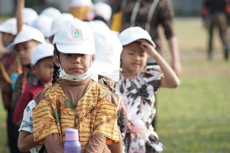 Foto de Lampung - 17 de agosto de 2023: Estudiantes de la escuela primaria indonesia usan batik y sombrero blanco en la ceremonia de izamiento de la bandera en conmemoración del día de la independencia de Indonesia - Imagen libre de derechos