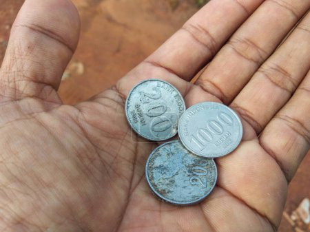 Close-up view of three coins of different values in a person's hand. Indonesian coins