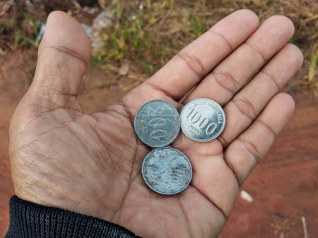 Nahaufnahme von drei Münzen mit unterschiedlichen Werten in der Hand einer Person. Indonesische Münzen