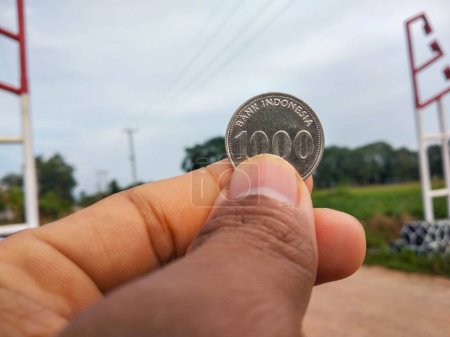 Foto de Un primer plano de una persona sosteniendo una moneda con el número 1000 rupias - Imagen libre de derechos