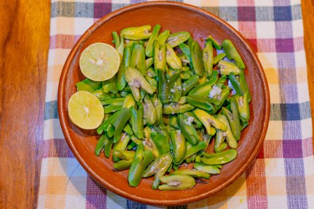 Foto de Semillas de Inga edulis, fruta exótica servida en un plato de barro acompañado de limón y sal. comúnmente llamado: guama, guaba, pacae o pacay - Imagen libre de derechos